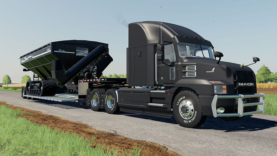 A black Mack Anthem hauling a low loader flatdeck. On the trailer, there's a grain cart